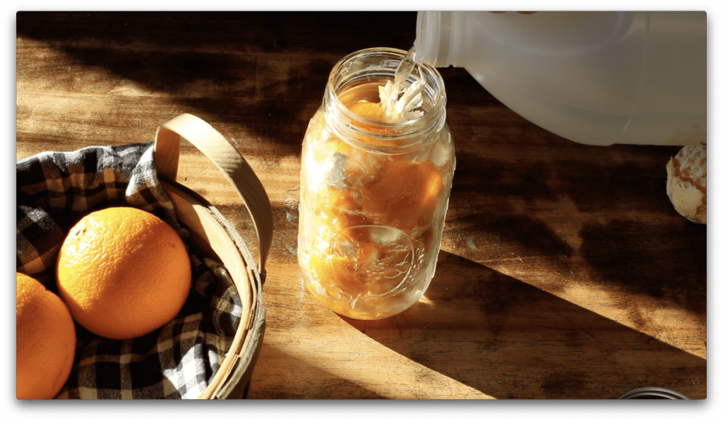 orange peels fill a mason jar. white vinegar is being poured over them to begin the infusion process.