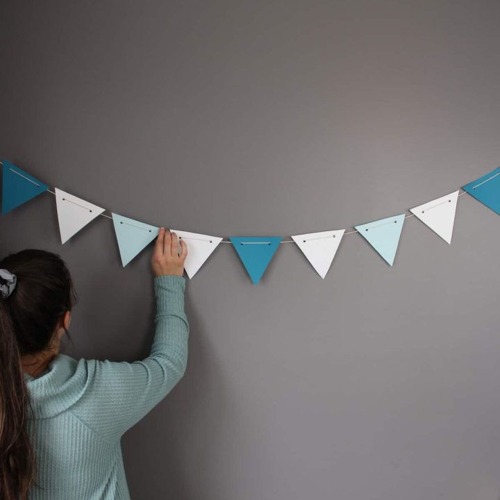 a woman in a light blue sweater with a pony tail held up by a grey scrunchie hangs party decor made of dark blue, light blue, and white card stock.