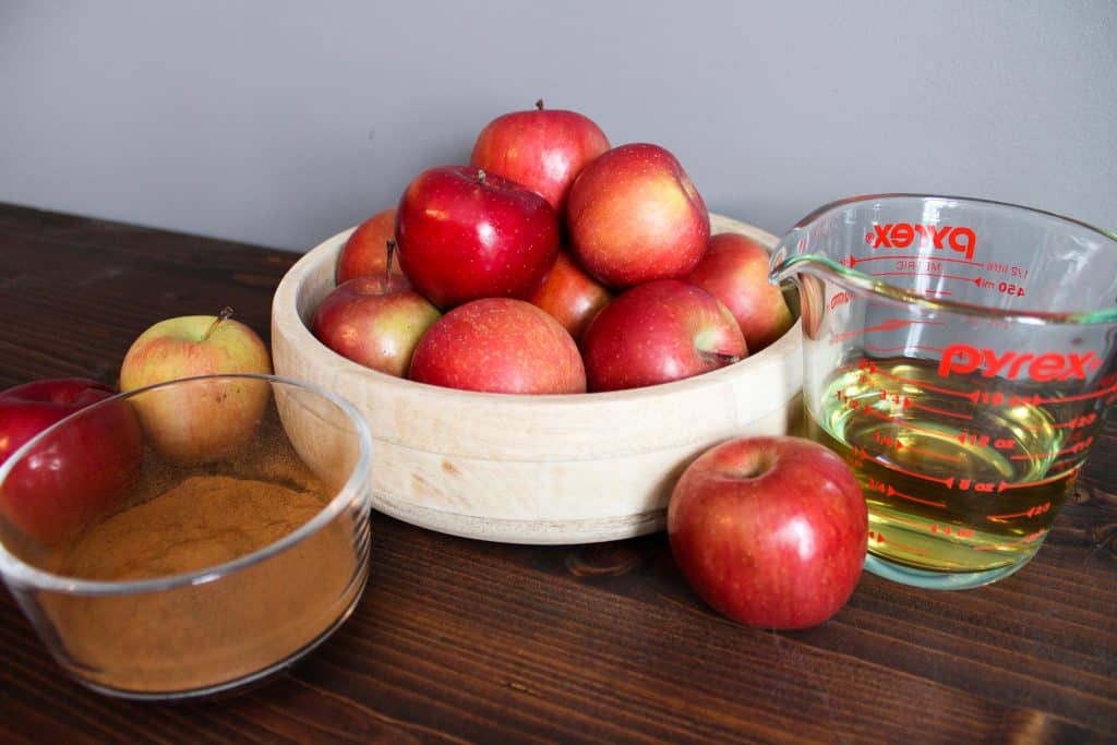 The ingredients needed for recipe 2 displayed in glass containers around the apples in a wooden bowl