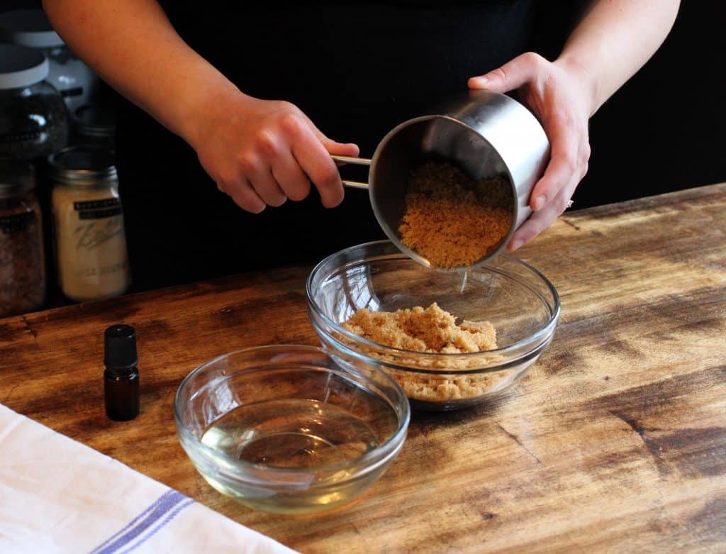 a woman pours brown sugar into a mixing bowl