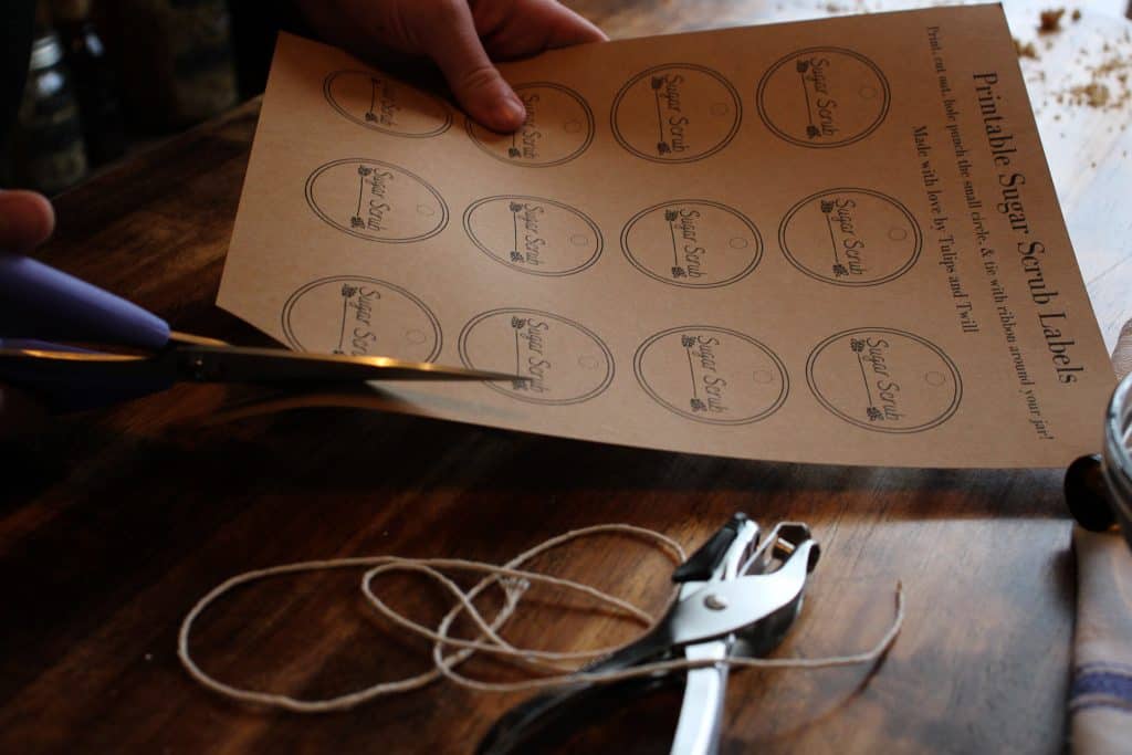 a sheet with printed labels is cut for use with scissors. some twine and a hole punch are also laid out on the table.