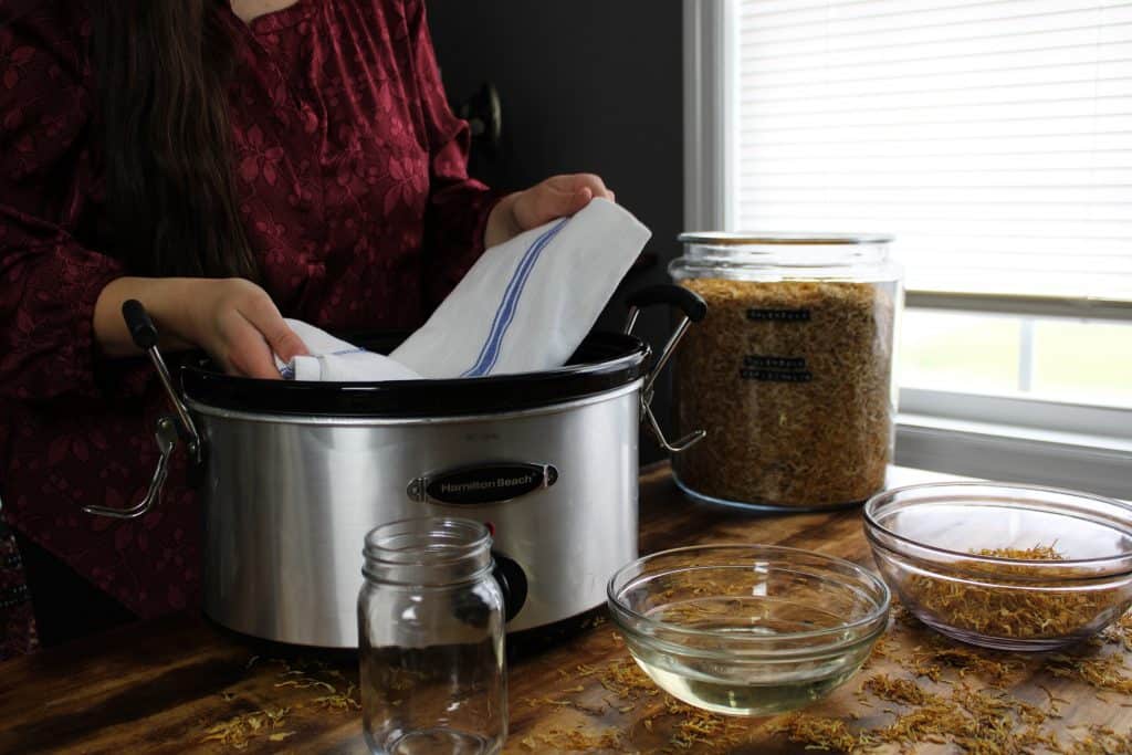 a woman in a maroon silk floral top places a kitchen towel into the bottom of the crockpot