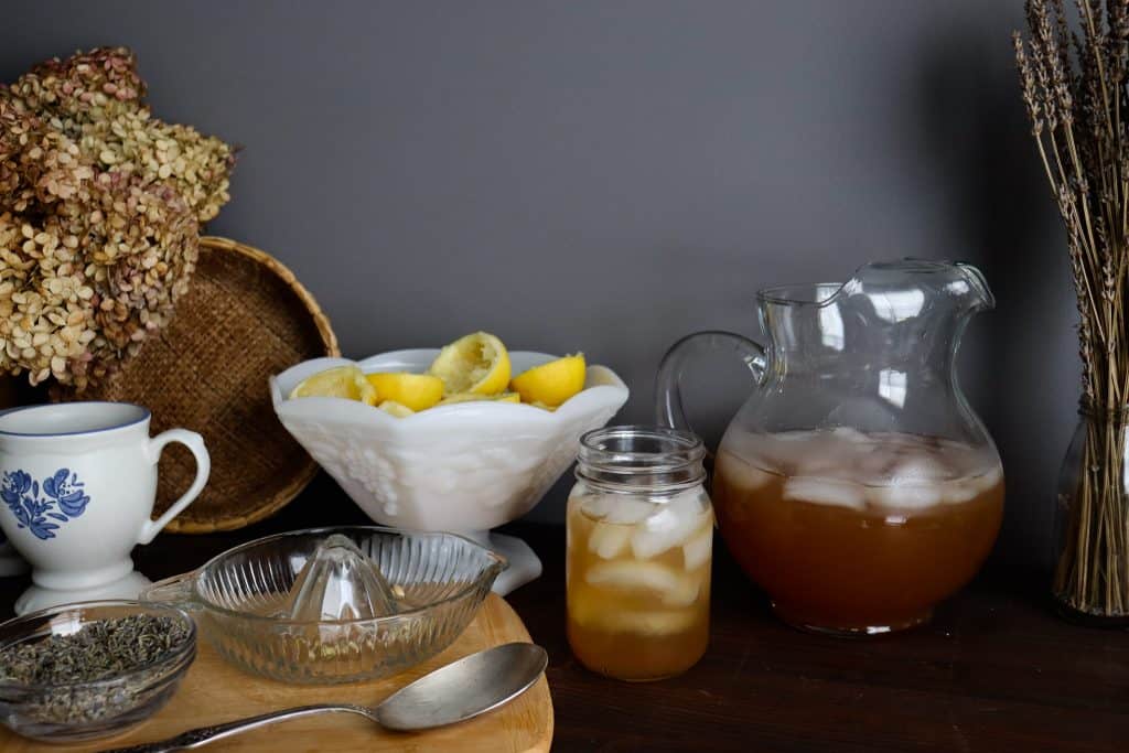 a glass of iced lavender honey lemonade on a table next to the ingredients and a pitcher