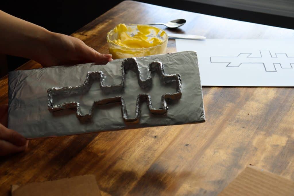 the cross shape and flat rectangular base are covered in tin foil and fastened together with some tape on the edges