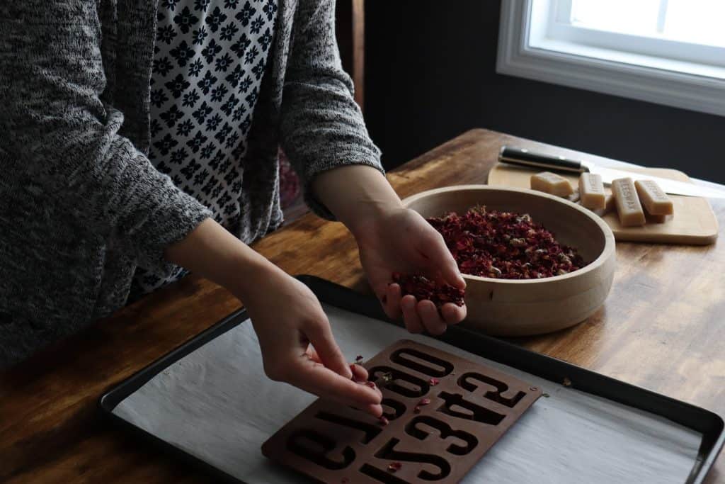 a woman adds dried rose petals to the mold