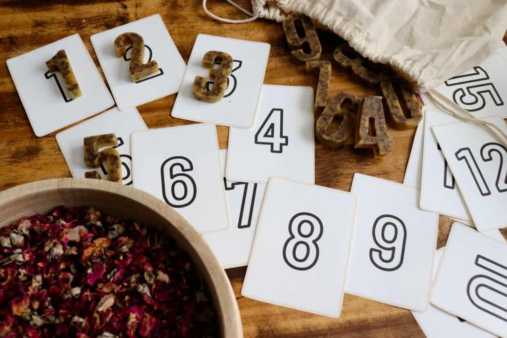 Beeswax numbers are in use with flashcards. They're stored in a canvas bag. There is a wooden bowl of dried roses nearby.