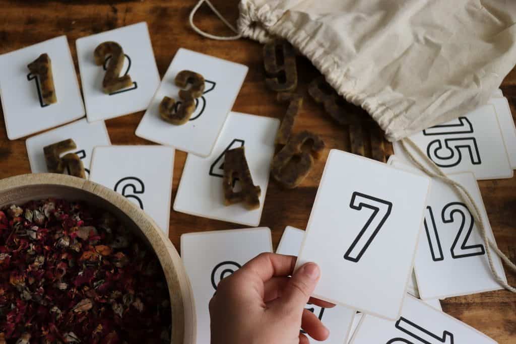 a woman's hand is holding a flashcard that says the number 7. Some cards are matched with numbers.
