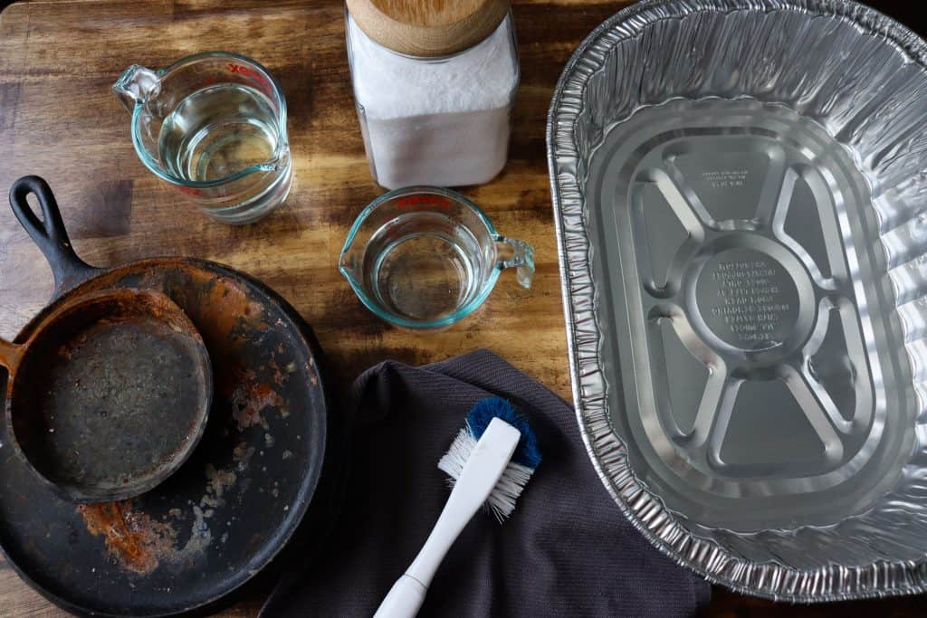left to right: rusty cast iron, water, vinegar, salt, scrub brush, towel, aluminum pan.