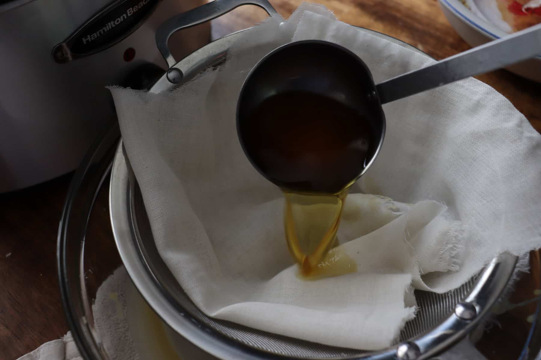 a ladle pouring beeswax through cheesecloth lined strainer