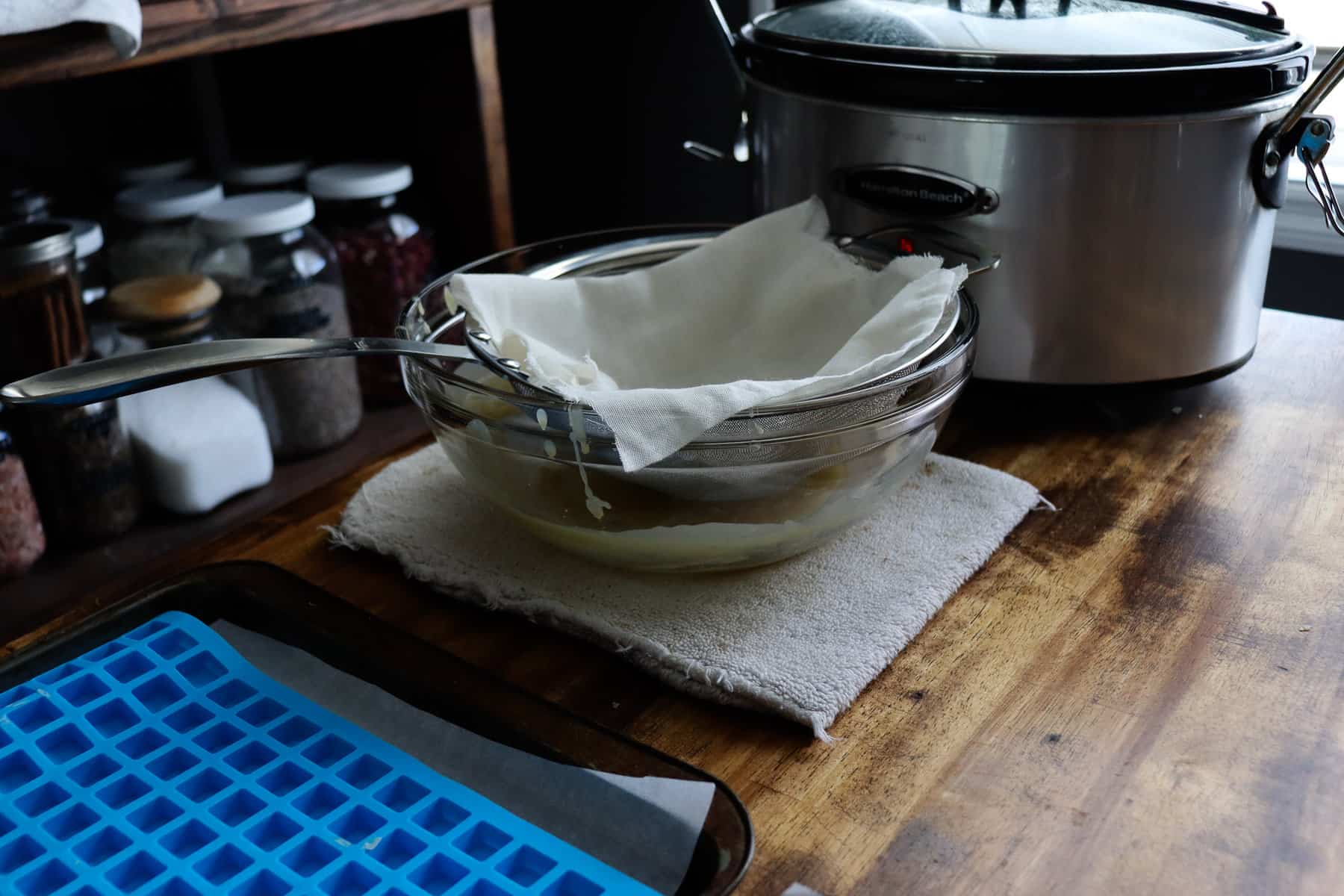 a glass bowl has a strainer lined with cheesecloth sitting on it ready to go