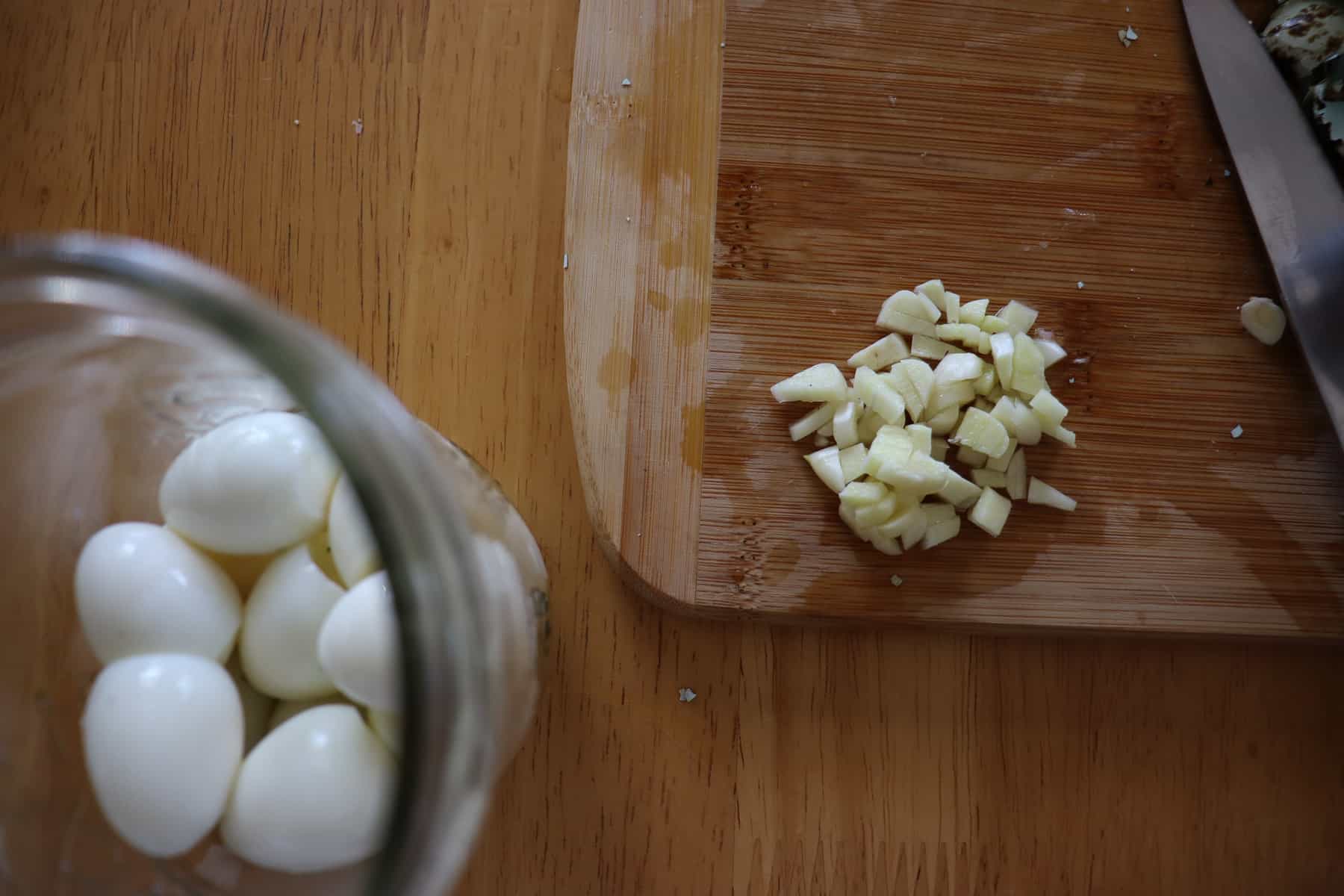 chopped garlic next to a jar of quail eggs and dill