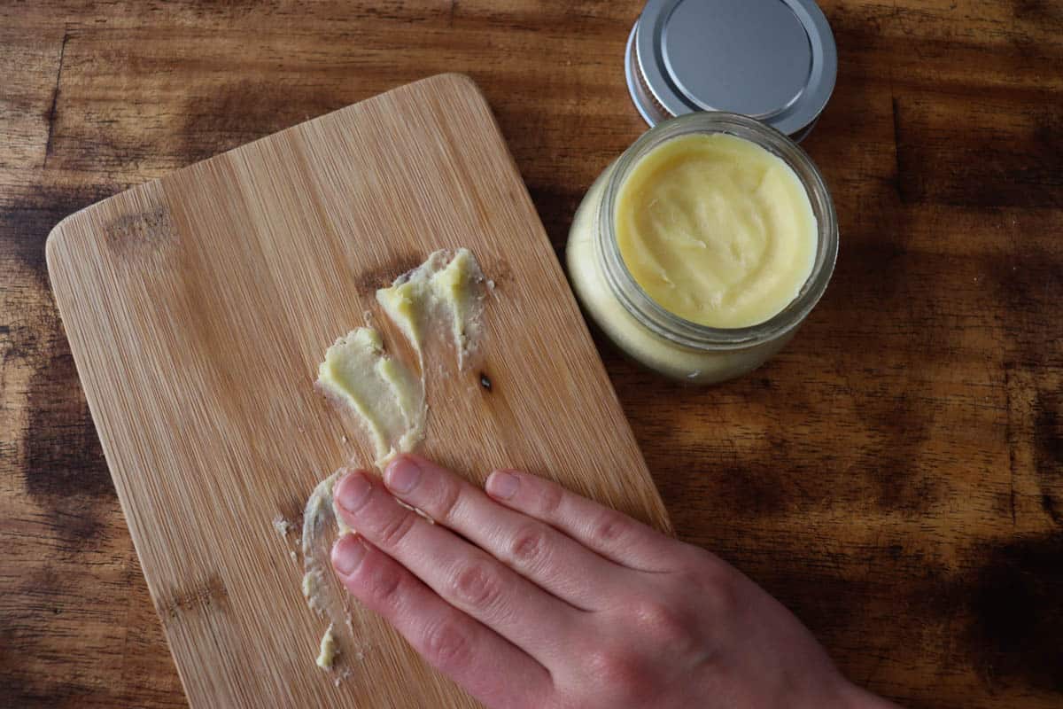 spreading board butter across a wooden cutting board. there is a jar of wood butter to the side