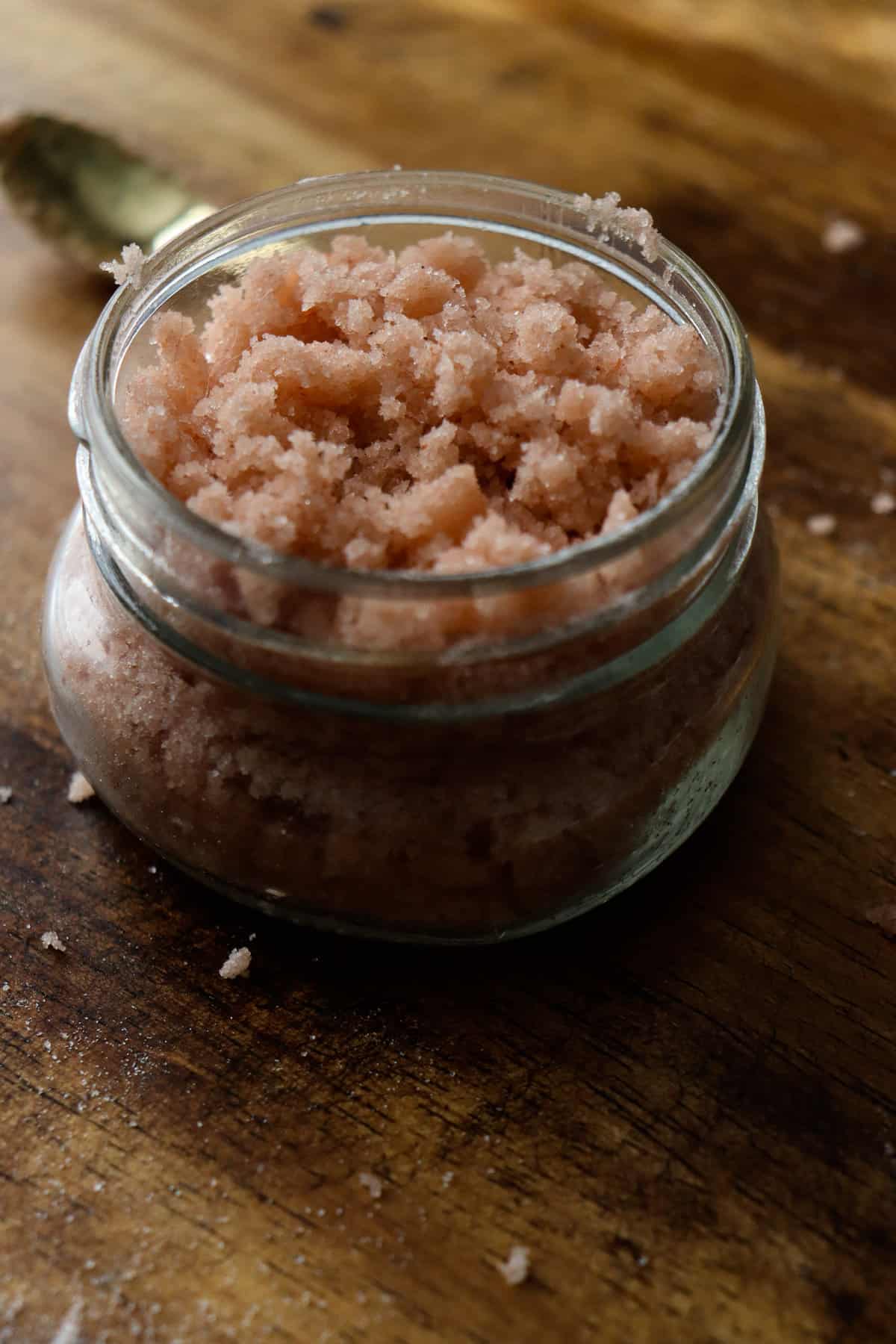 a pink salt scrub in a glass jar with a tiny golden spoon nearby