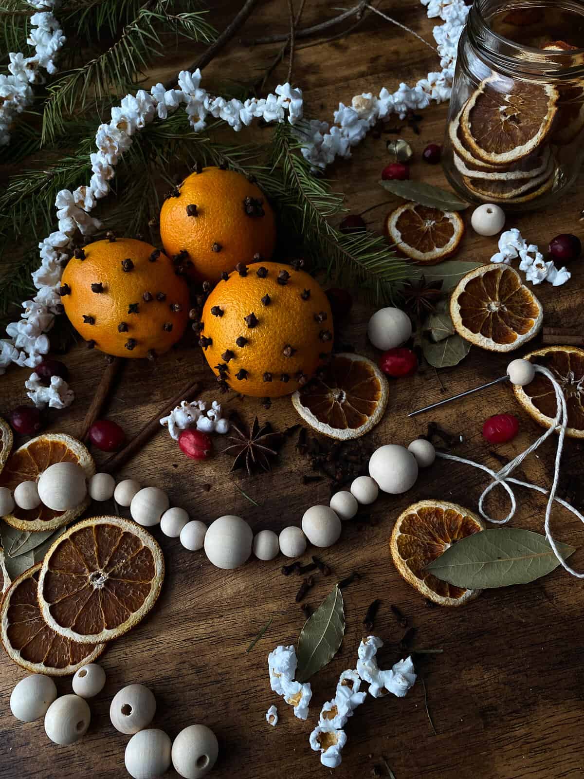 orange pomanders, wooden bead garland, popcorn garland, and so many crafting supplies all over a wooden work surface