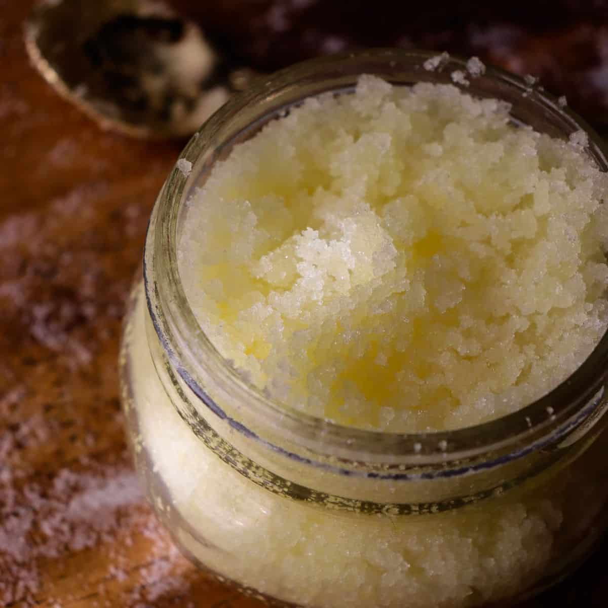 salt scrub with a yellow tint from jojoba oil in a glass jar with a tiny golden spoon nearby