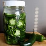 jalapeños in brine next to whole jalapeños on a cutting board