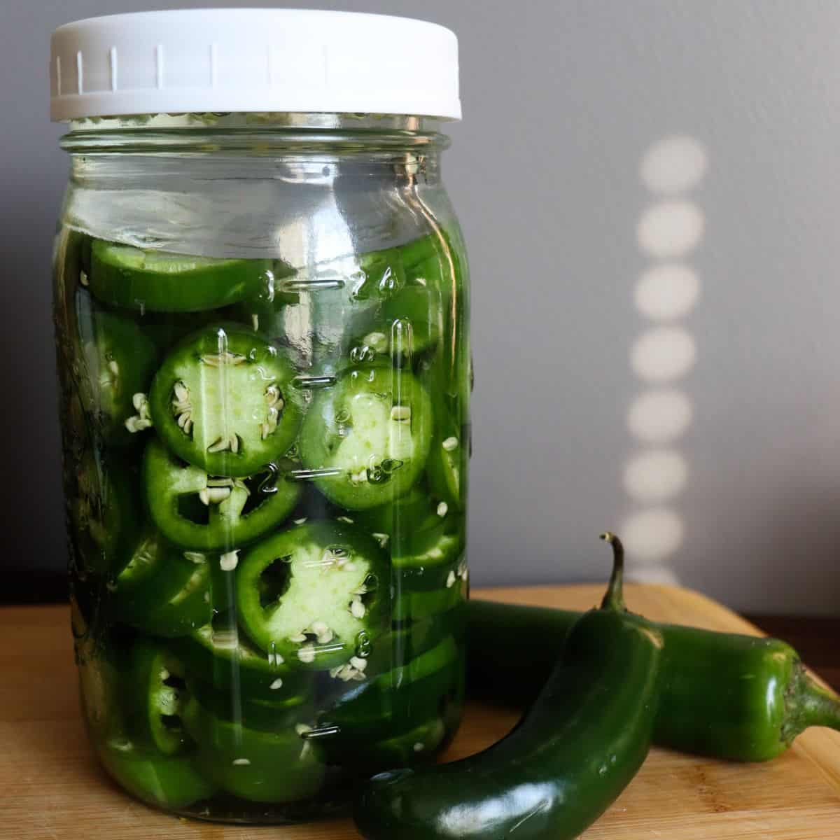 circular cut jalapenos in brine next to whole ones on a cutting board