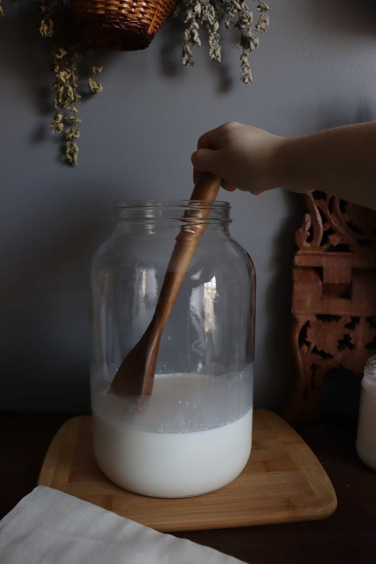 a woman using a wooden spoon to combine ingredients in a large glass jar
