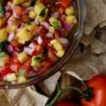 fresh made pico de gallo in a glass bowl surrounded by chips and roma tomatoes