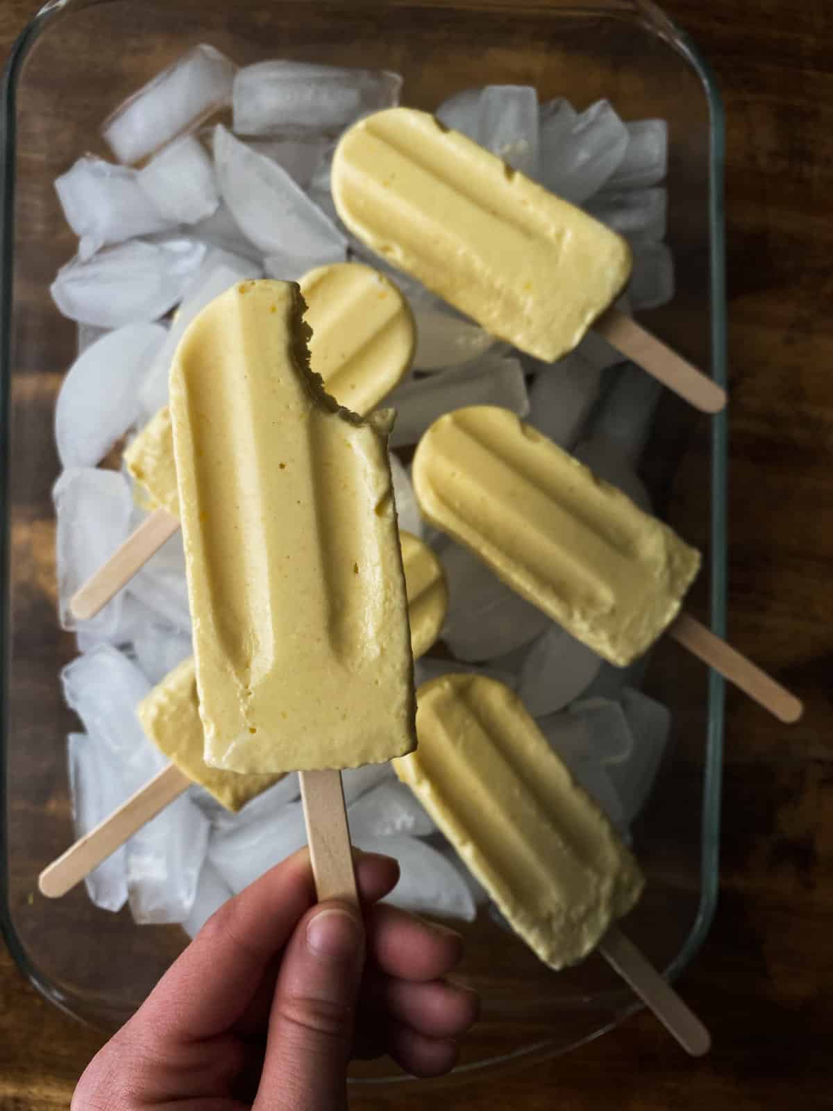 a woman holds a popsicle she took a bite out of. there are more laid out on ice!