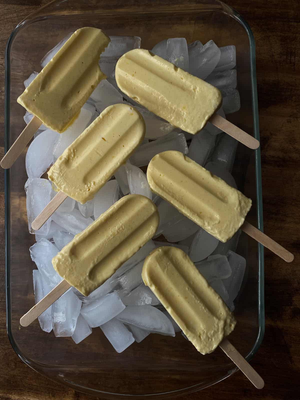 mango popsicles laid out on ice. one has a bite taken out of it!