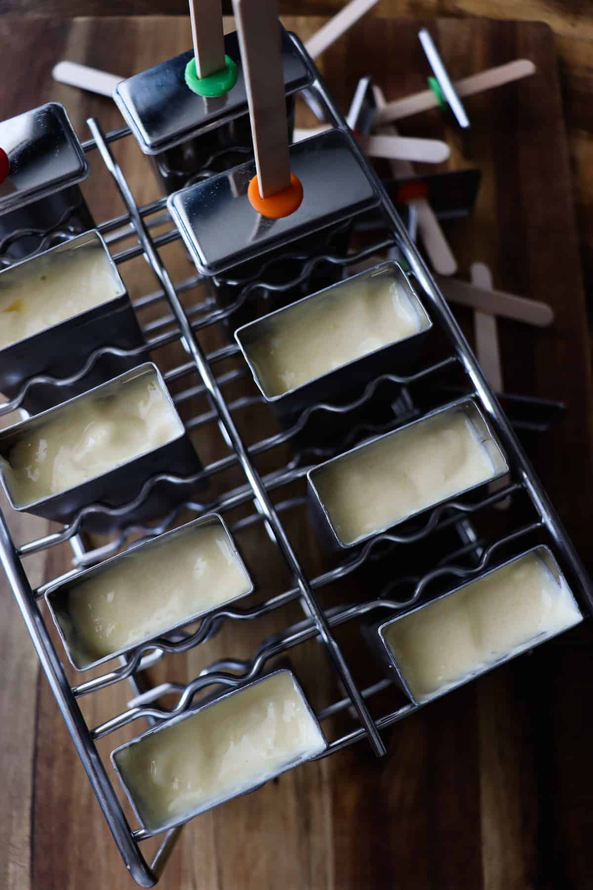stainless steel popsicle mold with homemade mango pops spooned into the openings. The tops and sticks are being placed on.