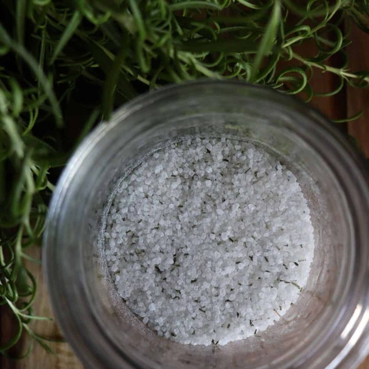 rosemary salt in a glass jar next to a lush rosemary plant