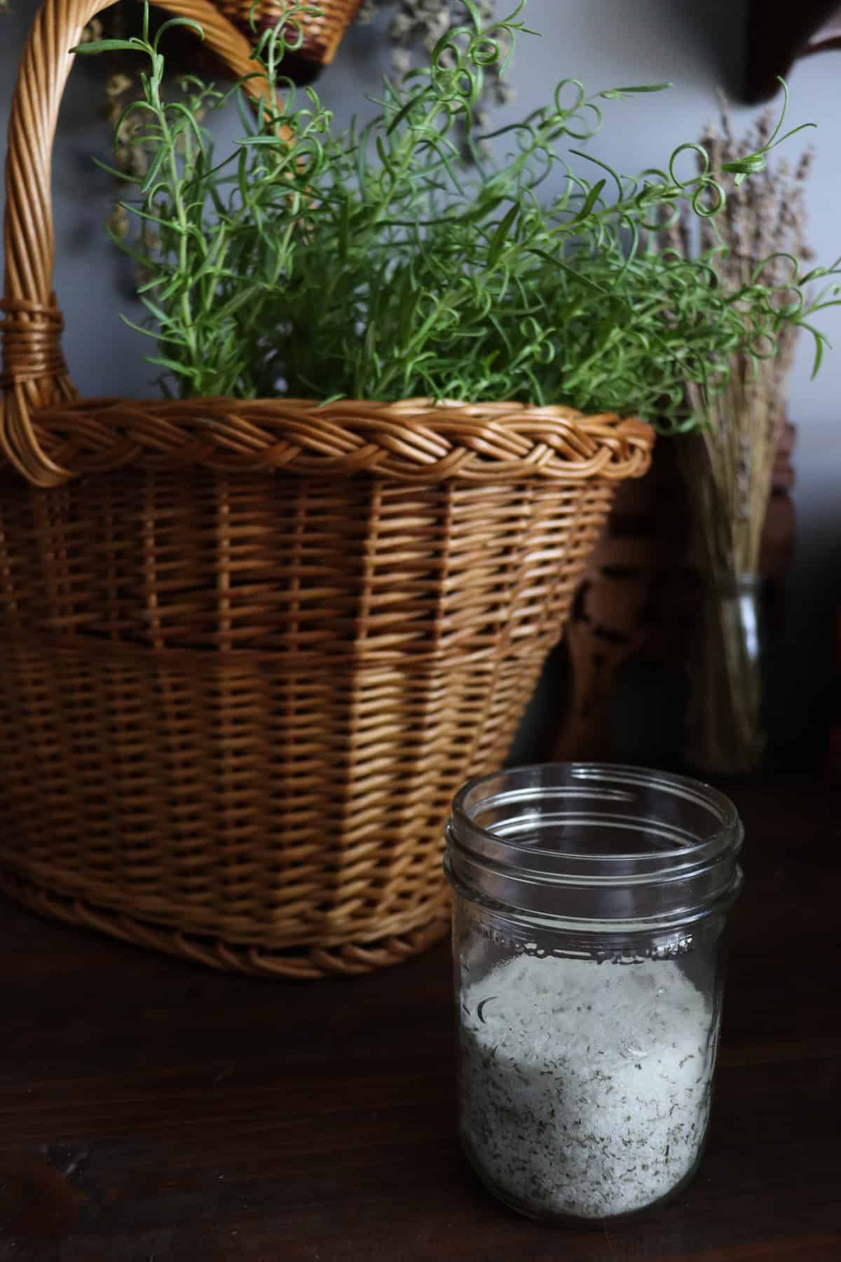 a woven basket overflowing with fresh rosemary next to a glass jar of rosemary salt!