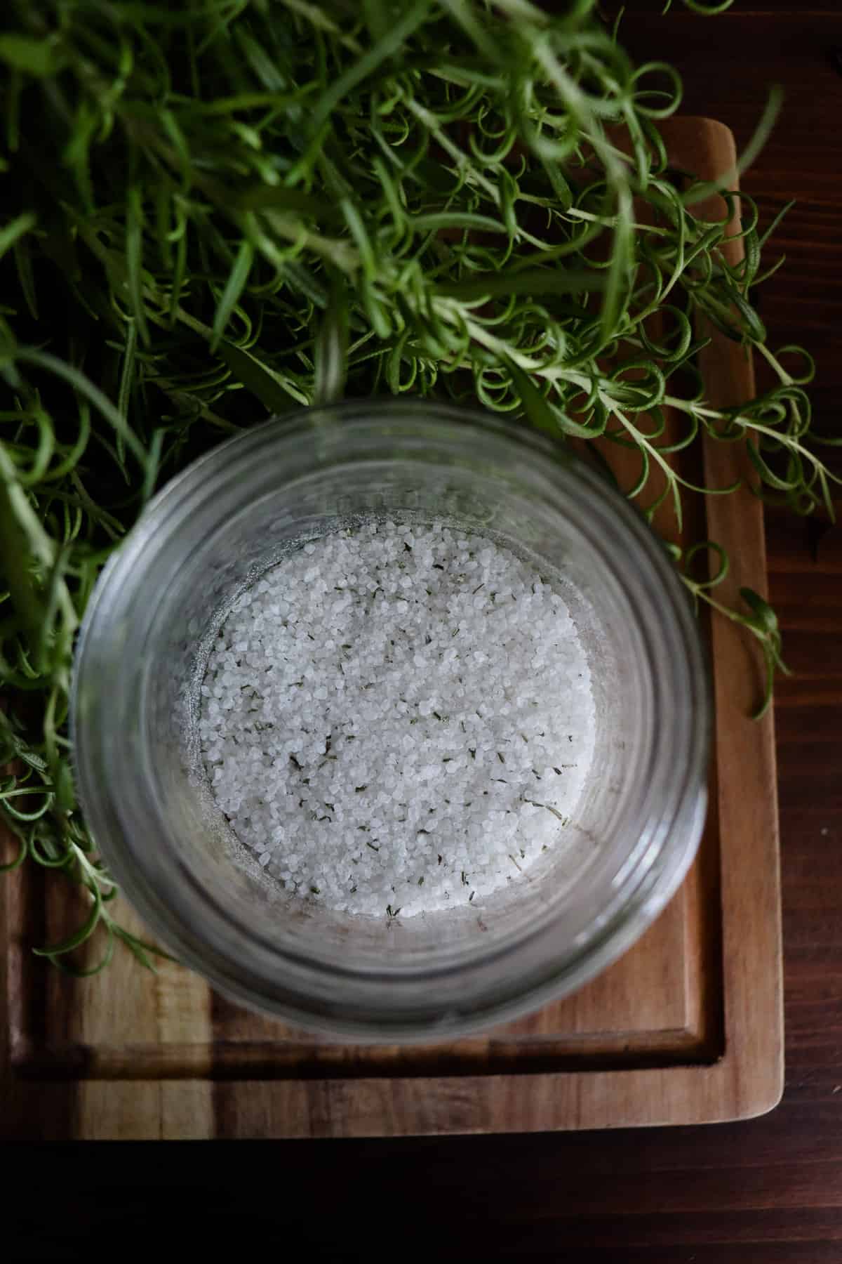 rosemary salt in a glass jar next to a lush rosemary plant on a wooden cutting board