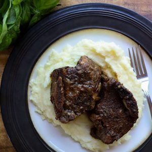 Beer braised short ribs served on some mashed potatoes on a white plate.