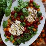 A platter of burrata caprese salad on a wooden table with tomatoes and fresh basil.