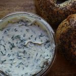 Chive and onion cream cheese on a wooden board with bagels to the side.